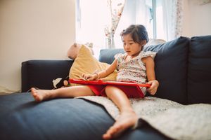 Lovely little girl reading an electronic book on the sofa happily.