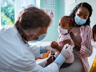 Pediatrician giving a young child a vaccination as her mother and sister looks on