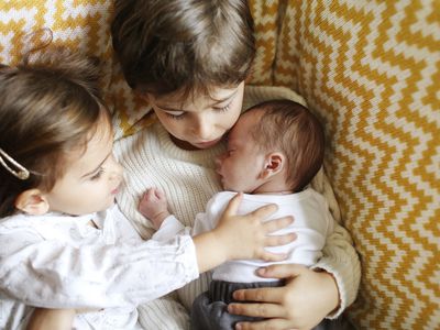 Two older siblings holding their new baby sibling