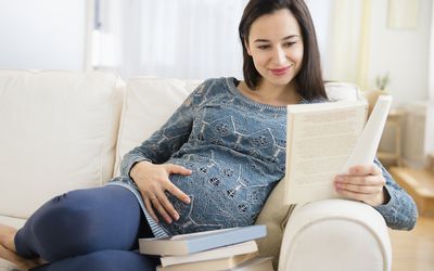 怀孕的白人妇女在沙发上看婴儿读物