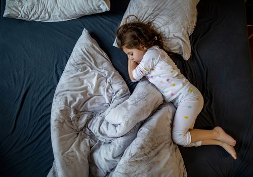 一个小女孩在床上睡觉，毯子和枕头都斜着