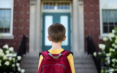 背着背包的小男孩站在学校大楼前