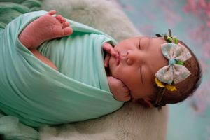 婴儿裹在绿色毯子里，头戴蝴蝶结和花箍