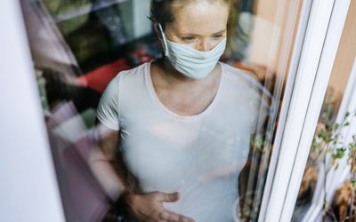 Pregnant woman with mask looking out window