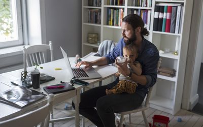 Father feeding baby boy while using laptop at home