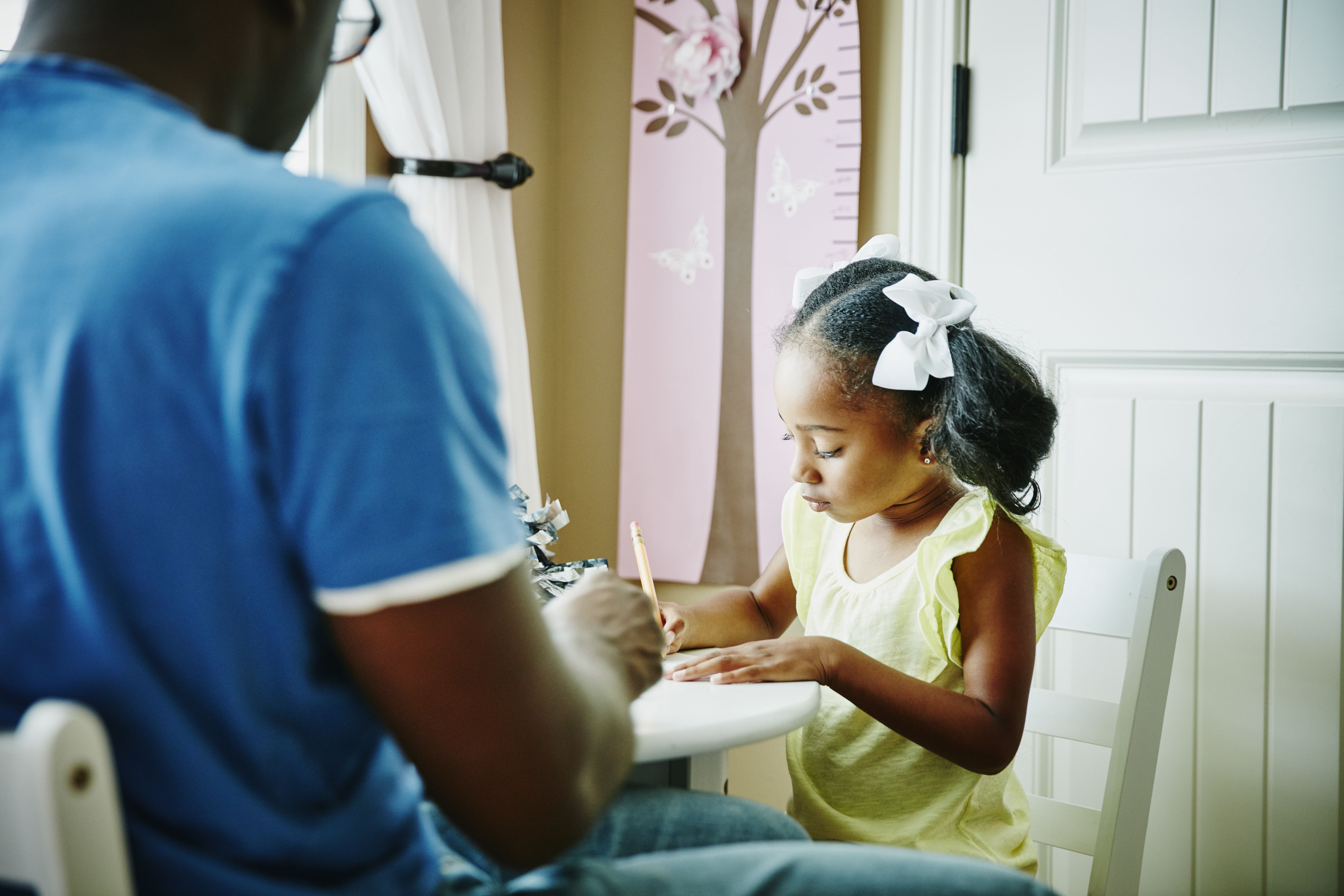 Girl writing while dad watches.