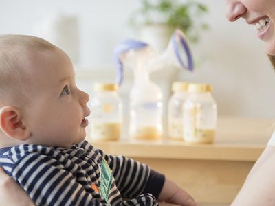 Mom holding baby with breast pump and bottles of milk in background