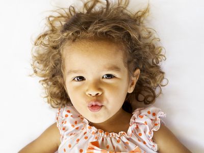 Girl wearing polka dots with curly brown hair and puckered lips looking at the camera