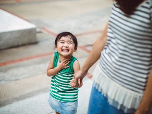 Smiling toddler holding hands with mom in park