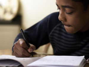 男孩(12-13岁)在书桌前做作业的特写