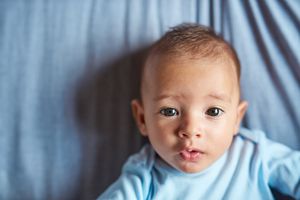 婴儿穿着蓝色的连体衣在蓝色的床单盯着镜头