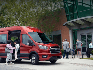 A red Ford Transit Van, with parents and kids walking into a gymnasium