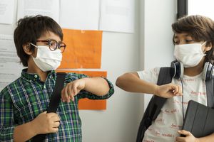 两个戴着口罩，拿着学习用品的学生撞肘。