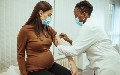 Pregnant woman prepares to receive vaccine by having her arm sanitized.