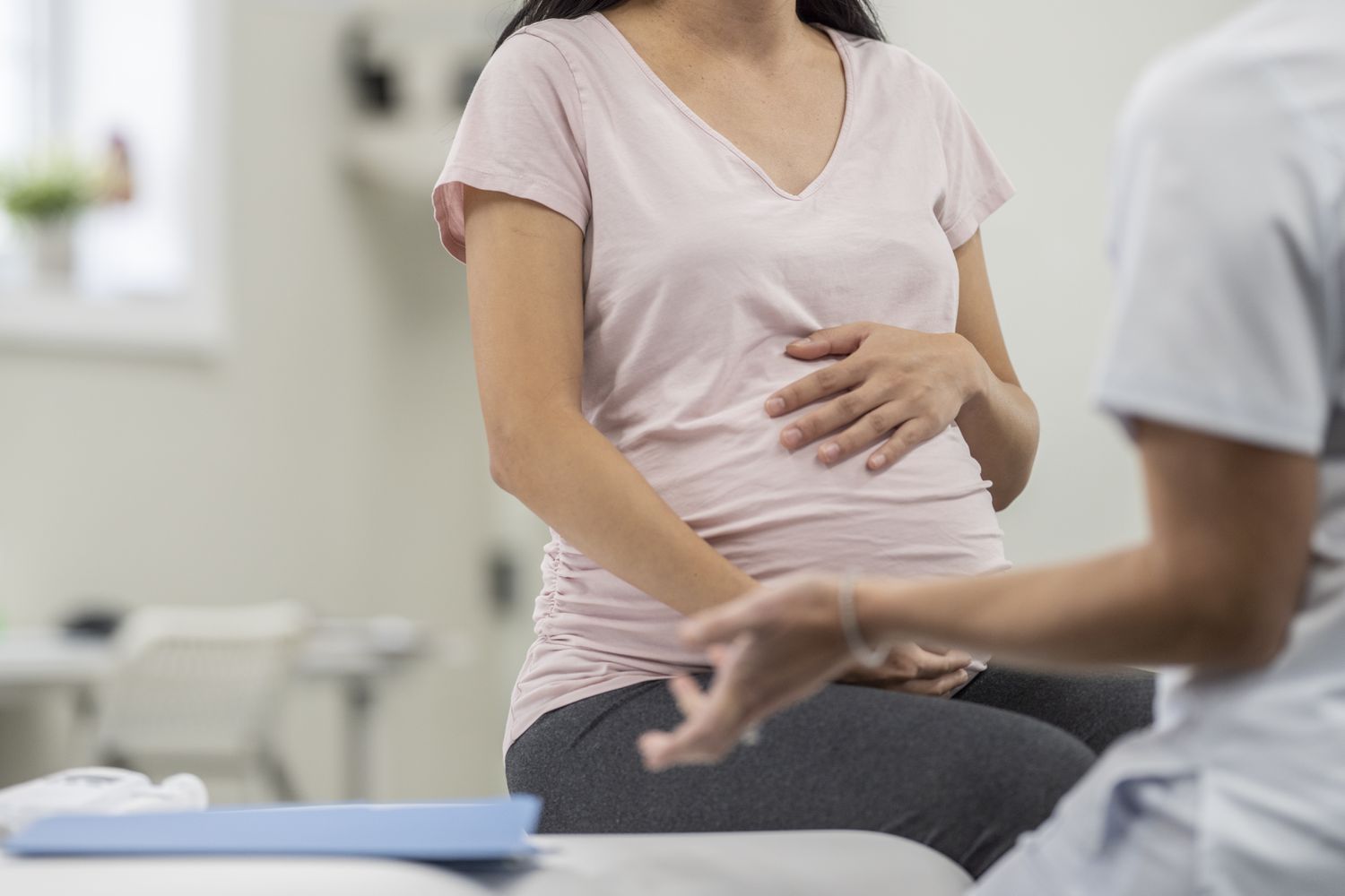 image of a pregnant person holding belly and sitting on a doctor's table