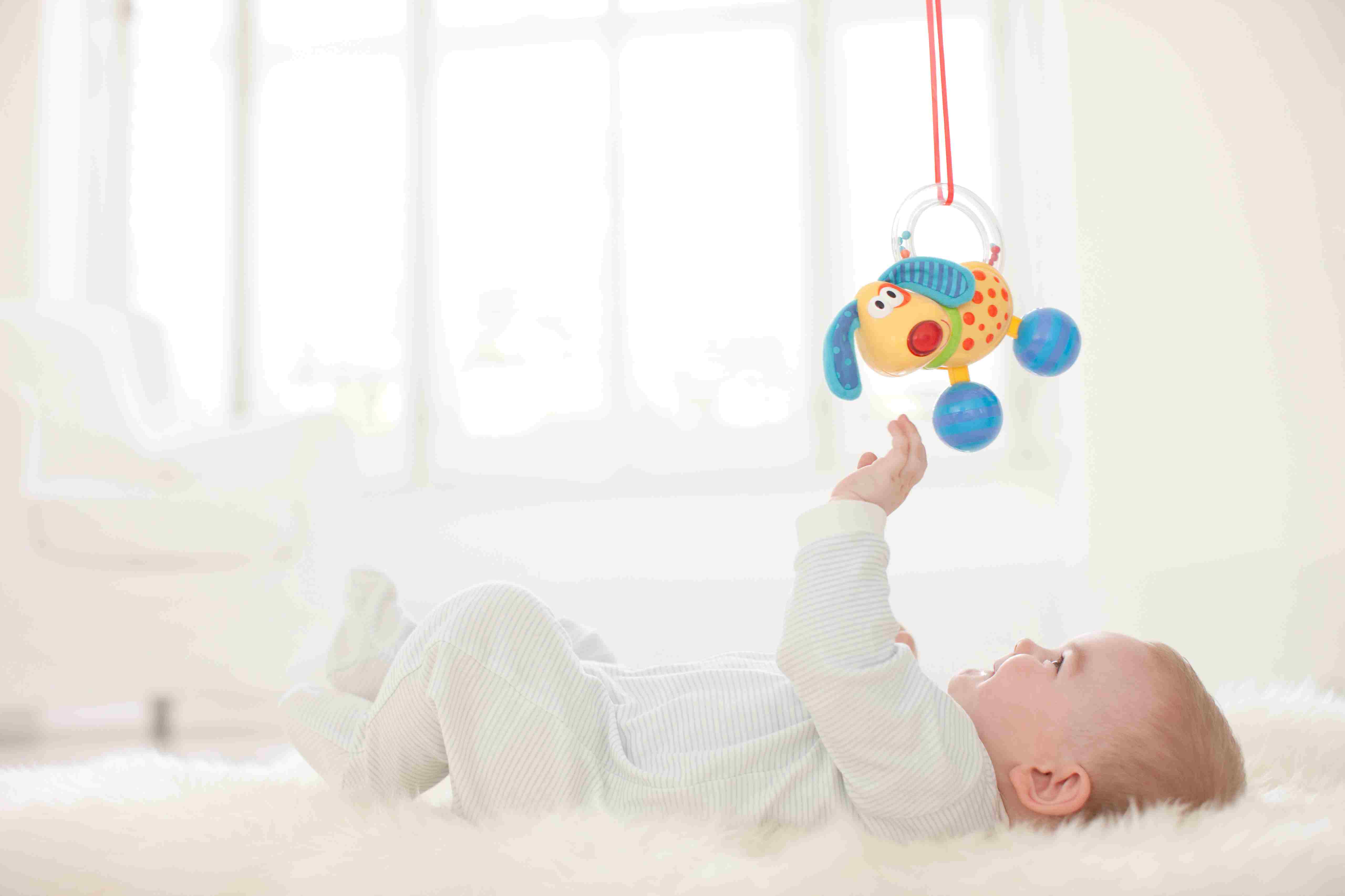地毯上的婴儿伸手去抓悬挂在头顶上的玩具