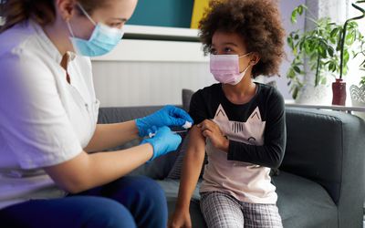 A young child gets vaccinated by a nurse on a couch.