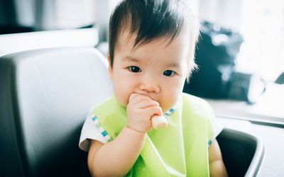 可爱的婴儿吃婴儿手指饼干在高椅子上存货照片