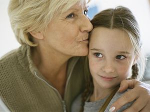 Senior woman with arm around granddaughter, kissing forehead, portrait