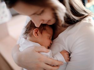 一个母亲抱着刚出生的儿子在家里的特写。年轻妇女满怀爱意地抱着她刚出生的男婴或女婴。