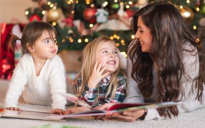 两个小妹妹和妈妈在客厅的圣诞树旁看书