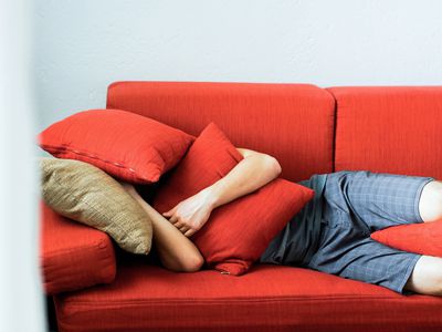 Teenage boy lying on couch with cushions over his face