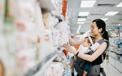 年轻的亚洲母亲抱着可爱的女婴在购物中心选购婴儿用品，正在看各种尿布