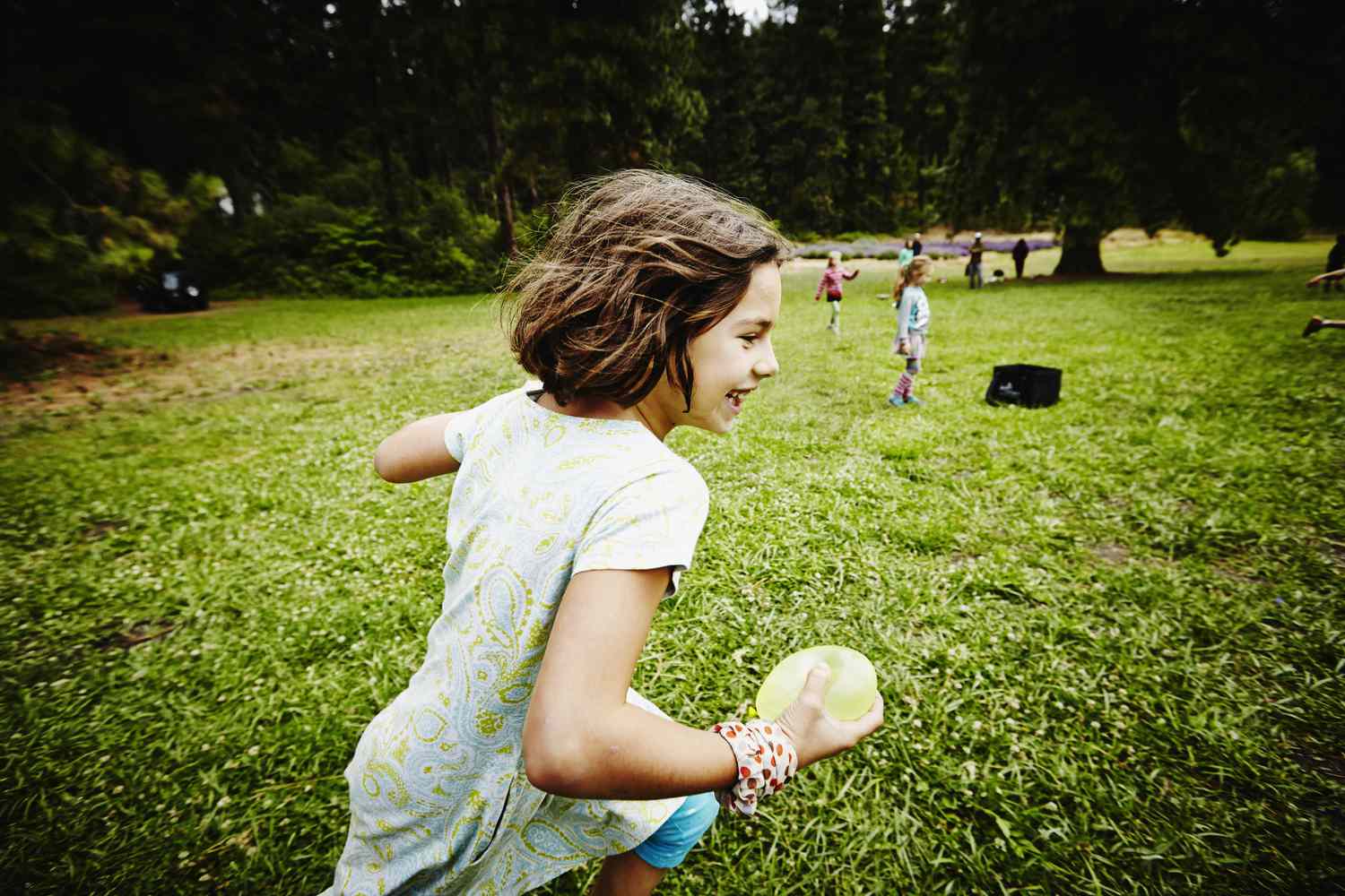 Girl running through field with water balloon