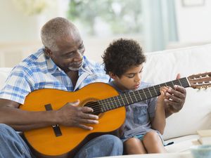 Boy playing guitar with grandfather on couch