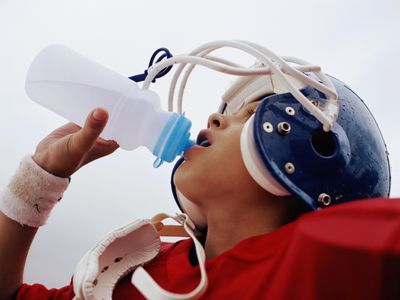 男孩(10-12) in football uniform drinking from water bottle, close up