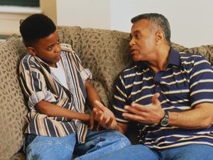 父亲正严肃地和坐在沙发上的儿子(11-13岁)说话