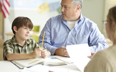 Boy (9-11) with father and female teacher, sitting at desk in classroom