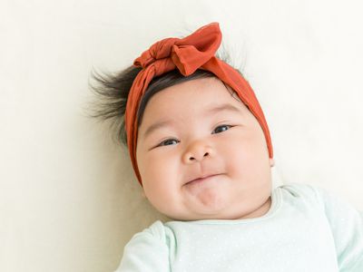 Baby girl with burnt orange headband and mint onesie looking at camera