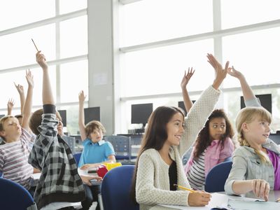 Students with hands raised in classroom.