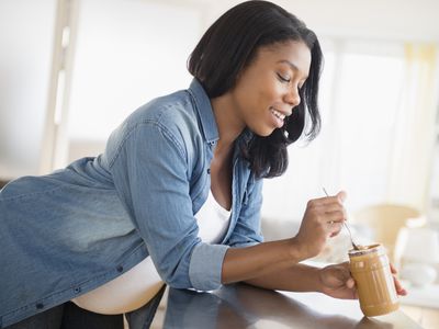 Black pregnant woman eating peanut butter in kitchen