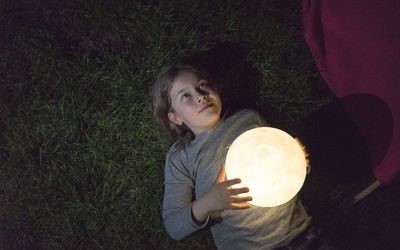 girl lying on a meadow holding a moon