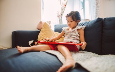 可爱的小女孩在沙发上开心地看电子书。