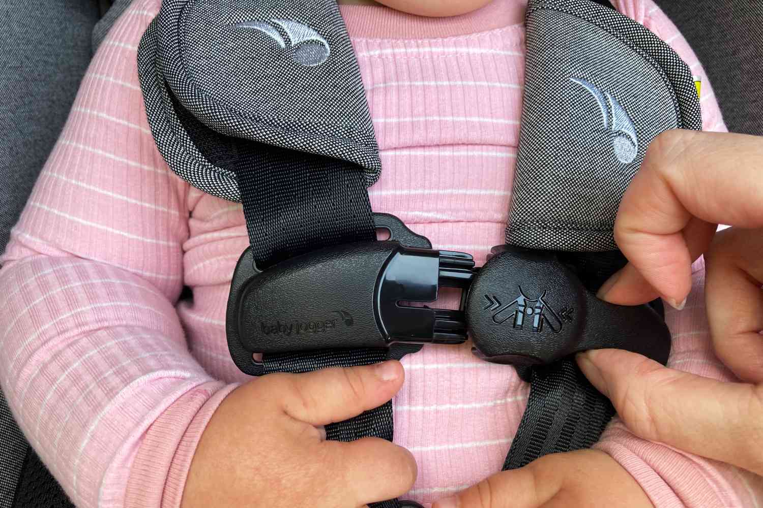 A woman secures a child into the Baby Jogger City Turn Rotating Convertible Car Seat