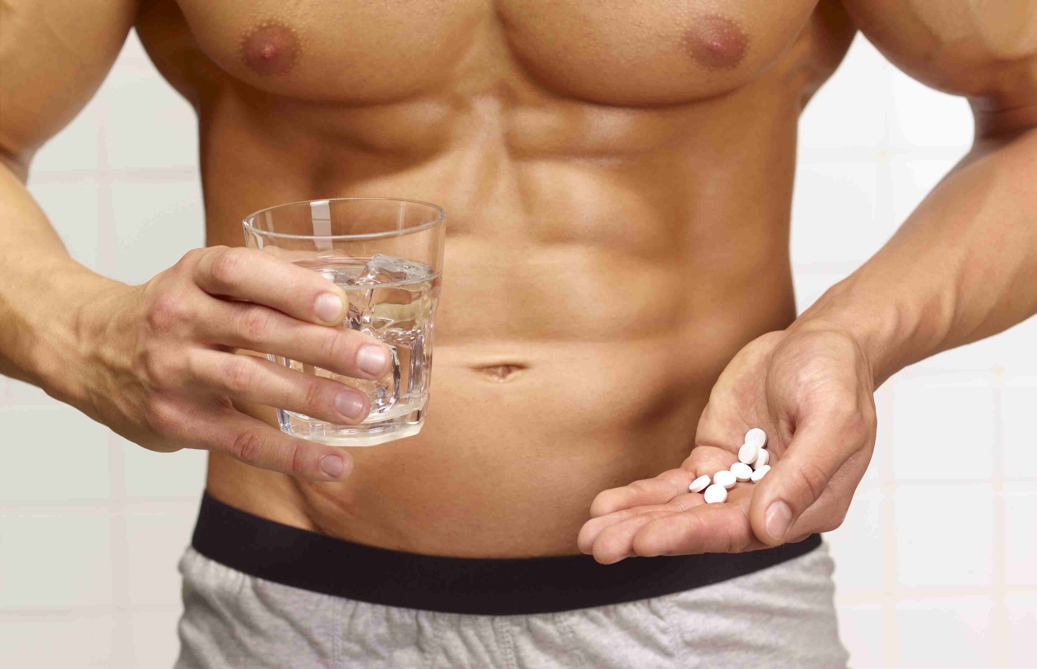 一个肌肉粗壮，腹肌六块的男人，手里拿着一杯水和一把合成代谢类固醇药片