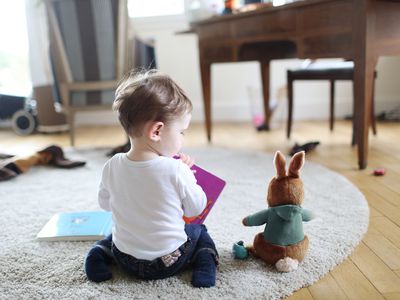 A baby boy reading book to his stuffed rabbit