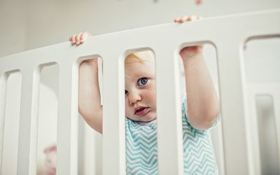 Baby standing in a white crib.