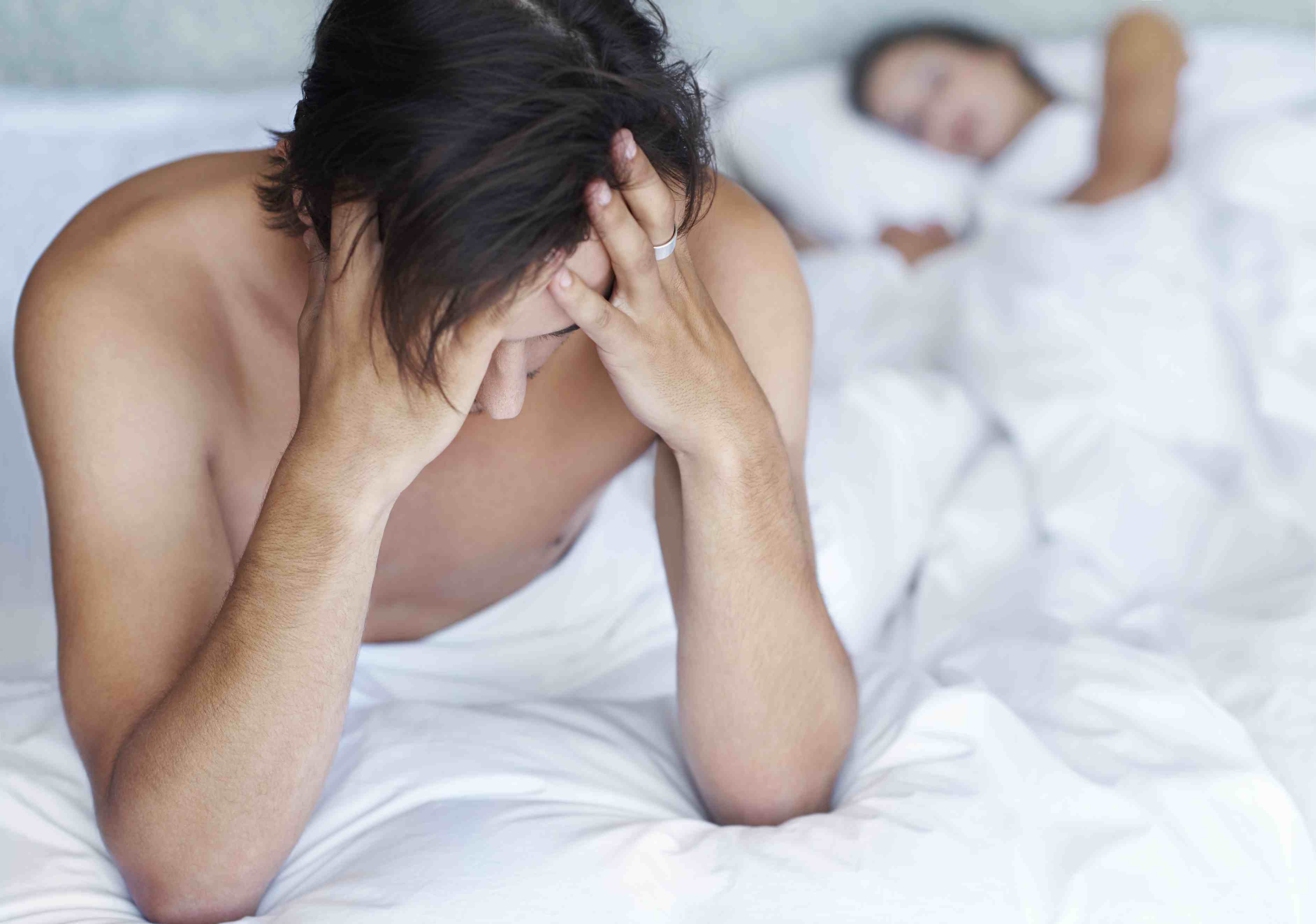 男人双手抱着头坐在床底，由于怀孕压力而导致勃起功能障碍