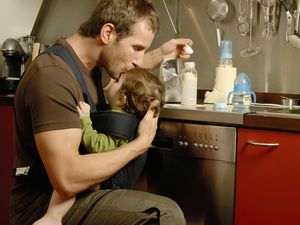 父亲抱着7-9个月大的儿子在厨房里准备牛奶