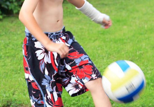 手臂上缠着石膏的男孩在踢足球