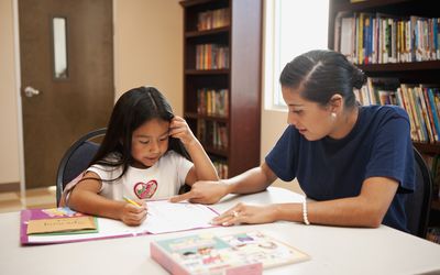 Hispanic woman helping girl with homework in library