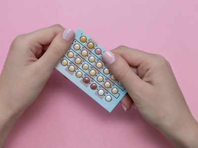 Close-Up Of Cropped Hands Holding Blister Pack Over Colored Background