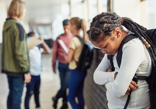 在学校的走廊上，一个被同龄人排斥在外的小女孩看起来很悲伤