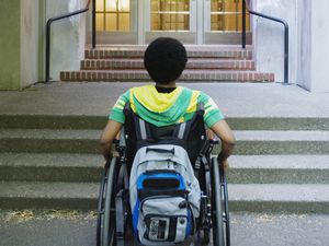 一位残疾学生站在学校门口。