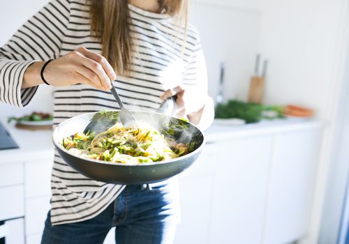 年轻女子拿着平底锅和素食意大利面