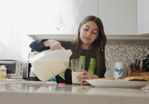 一个小女孩正在厨房里倒一杯牛奶